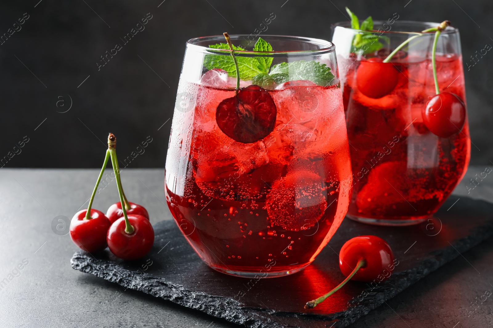 Tasty cherry soda with ice cubes, berries and mint in glasses on grey table, closeup Photo of Tasty cherry soda with ice cubes, berries and mint in glasses on grey table, closeup