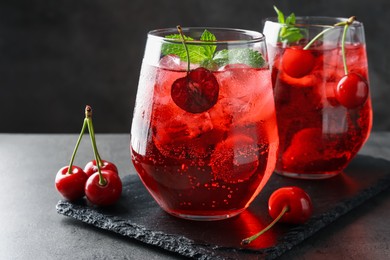 Photo of Tasty cherry soda with ice cubes, berries and mint in glasses on grey table, closeup