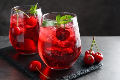 Photo of Tasty cherry soda with ice cubes, berries and mint in glasses on grey table, closeup