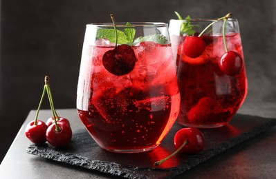 Photo of Tasty cherry soda with ice cubes, berries and mint in glasses on grey table, closeup