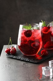 Photo of Tasty cherry soda with ice cubes, berries and mint in glasses on grey table, closeup