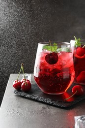 Photo of Tasty cherry soda with ice cubes, berries and mint in glasses on grey table, closeup
