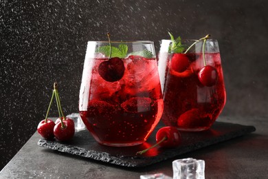 Photo of Tasty cherry soda with ice cubes, berries and mint in glasses on grey table, closeup