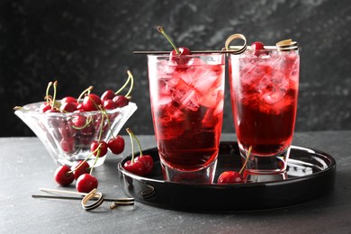 Photo of Tasty cherry soda with ice cubes and berries in glasses on grey table, closeup