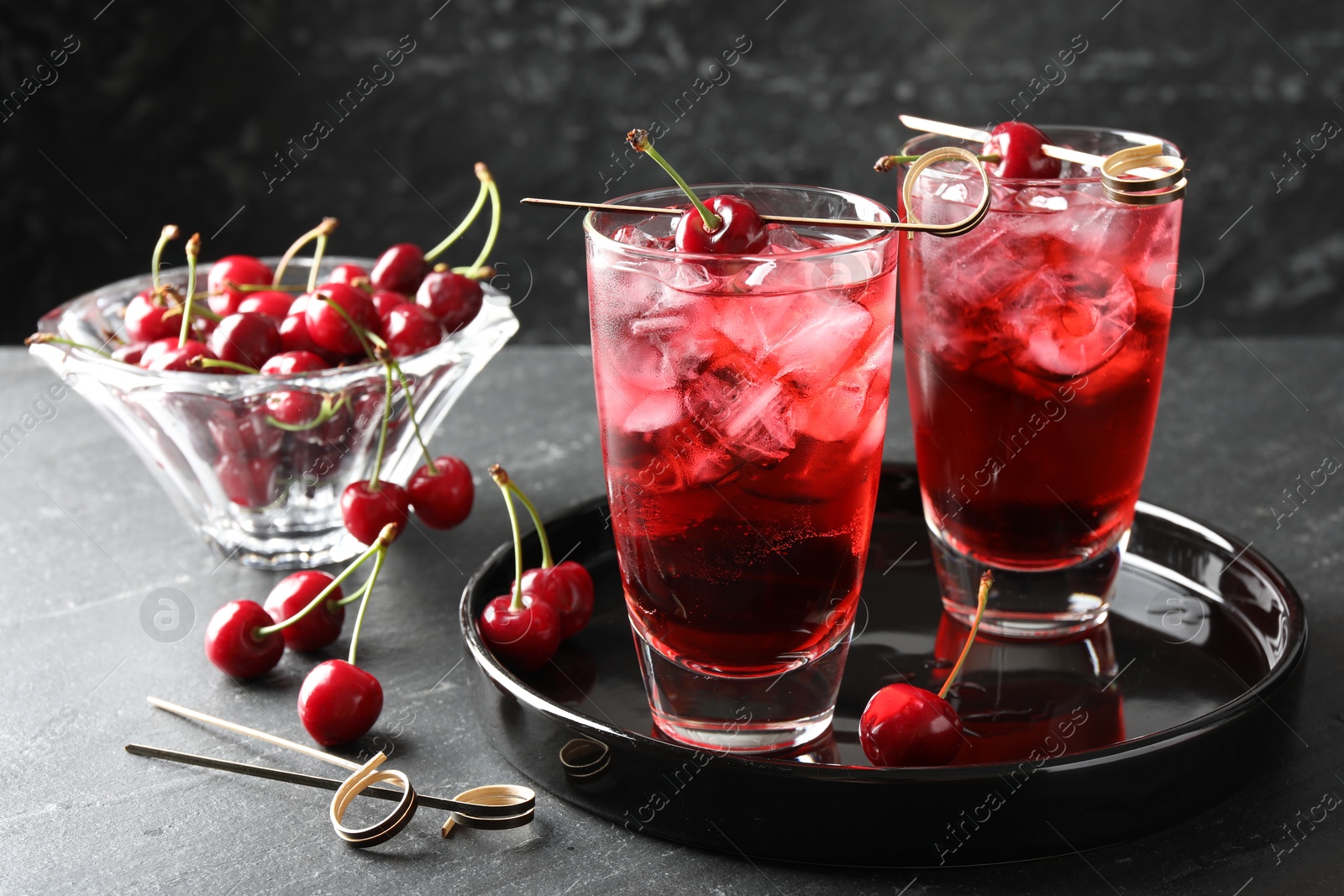 Tasty cherry soda with ice cubes and berries in glasses on grey table, closeup Photo of Tasty cherry soda with ice cubes and berries in glasses on grey table, closeup