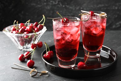 Photo of Tasty cherry soda with ice cubes and berries in glasses on grey table, closeup