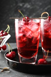 Photo of Tasty cherry soda with ice cubes and berries in glasses on grey table, closeup
