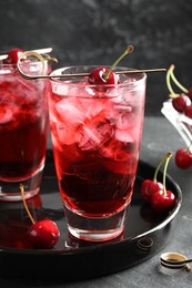 Photo of Tasty cherry soda with ice cubes and berries in glasses on grey table, closeup