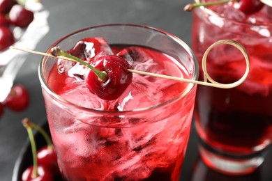 Photo of Tasty cherry soda with ice cubes and berries in glasses on grey table, closeup