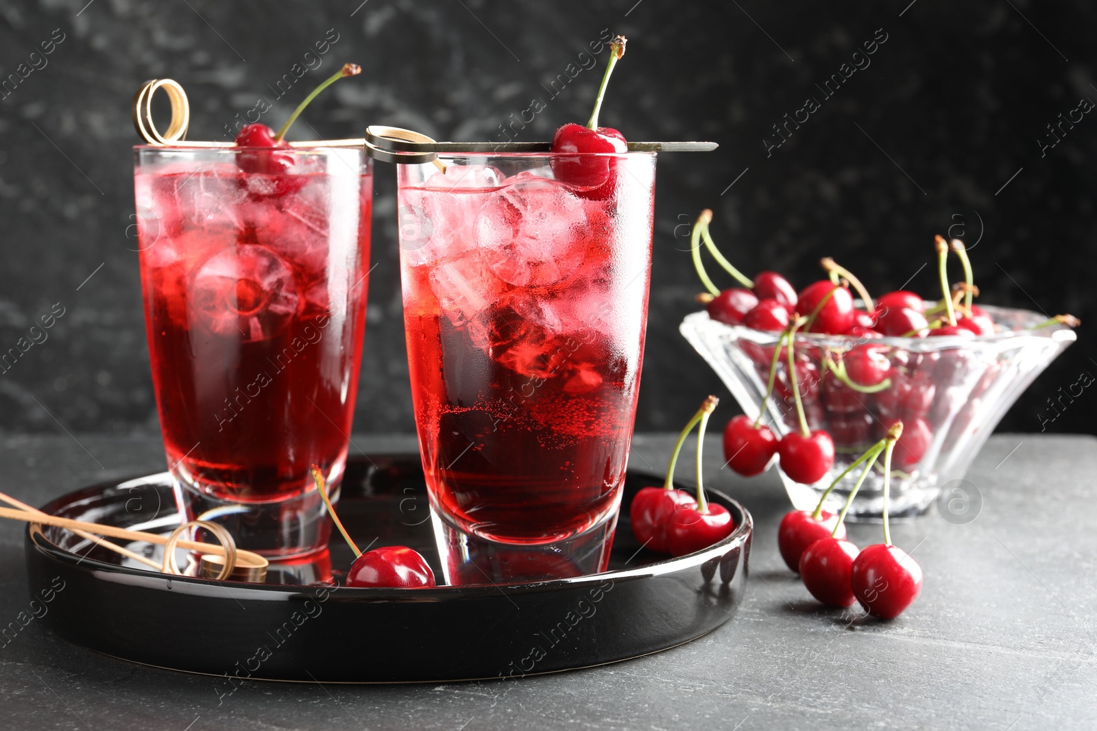 Tasty cherry soda with ice cubes and berries in glasses on grey table, closeup Photo of Tasty cherry soda with ice cubes and berries in glasses on grey table, closeup
