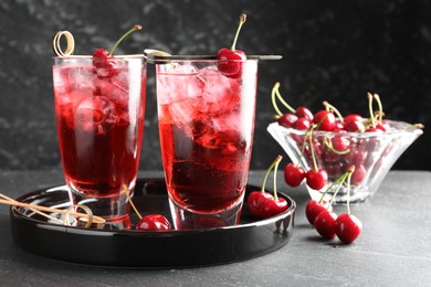 Photo of Tasty cherry soda with ice cubes and berries in glasses on grey table, closeup