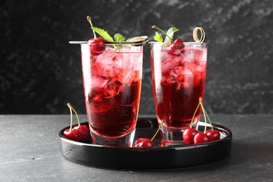Photo of Tasty cherry soda with ice cubes, berries and mint in glasses on grey table, closeup