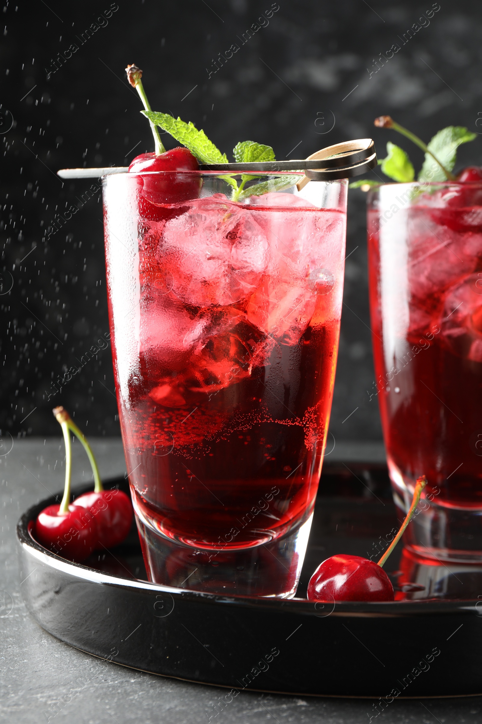 Tasty cherry soda with ice cubes, berries and mint in glasses on grey table, closeup Photo of Tasty cherry soda with ice cubes, berries and mint in glasses on grey table, closeup