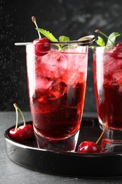Photo of Tasty cherry soda with ice cubes, berries and mint in glasses on grey table, closeup