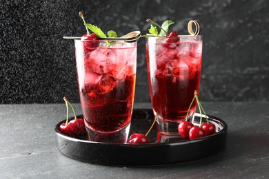 Photo of Tasty cherry soda with ice cubes, berries and mint in glasses on grey table, closeup