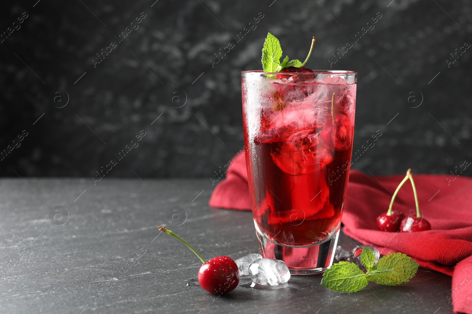 Tasty cherry soda with ice cubes, berries and mint in glass on grey table, closeup. Space for text Photo of Tasty cherry soda with ice cubes, berries and mint in glass on grey table, closeup. Space for text