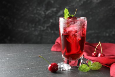 Photo of Tasty cherry soda with ice cubes, berries and mint in glass on grey table, closeup. Space for text