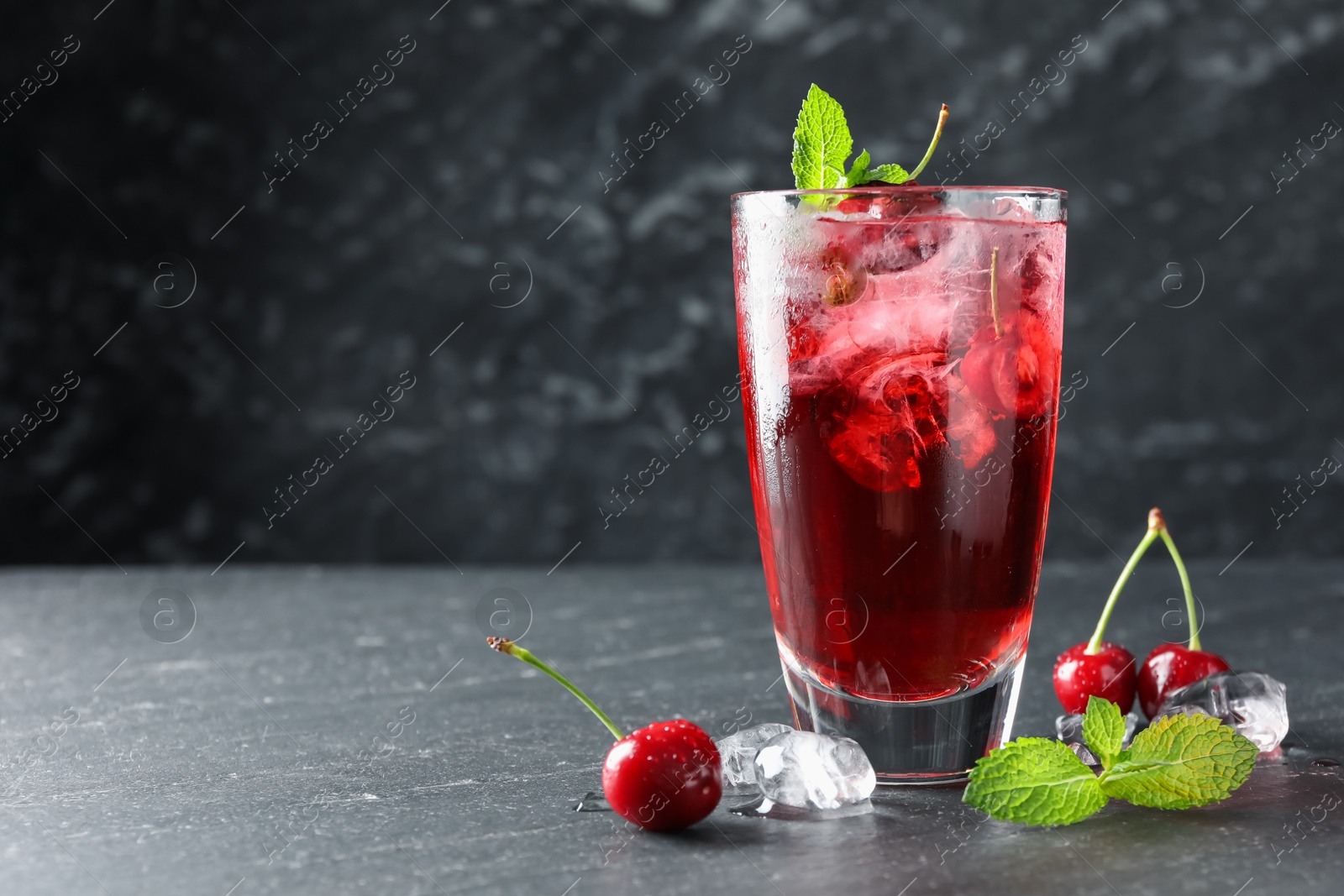 Tasty cherry soda with ice cubes, berries and mint in glass on grey table, closeup. Space for text Photo of Tasty cherry soda with ice cubes, berries and mint in glass on grey table, closeup. Space for text