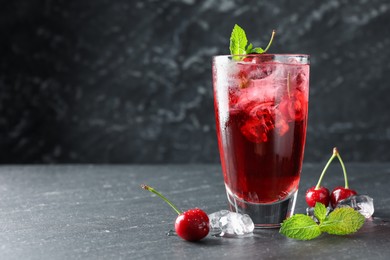 Photo of Tasty cherry soda with ice cubes, berries and mint in glass on grey table, closeup. Space for text