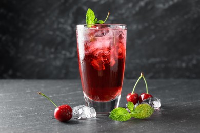 Photo of Tasty cherry soda with ice cubes, berries and mint in glass on grey table, closeup