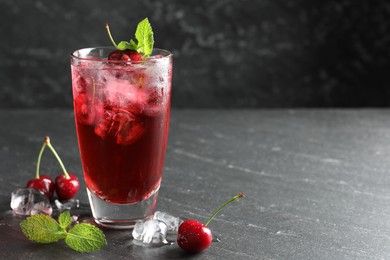 Photo of Tasty cherry soda with ice cubes, berries and mint in glass on grey table, closeup. Space for text