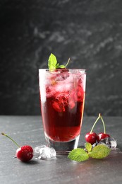 Photo of Tasty cherry soda with ice cubes, berries and mint in glass on grey table, closeup