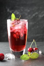 Photo of Tasty cherry soda with ice cubes, berries and mint in glass on grey table, closeup