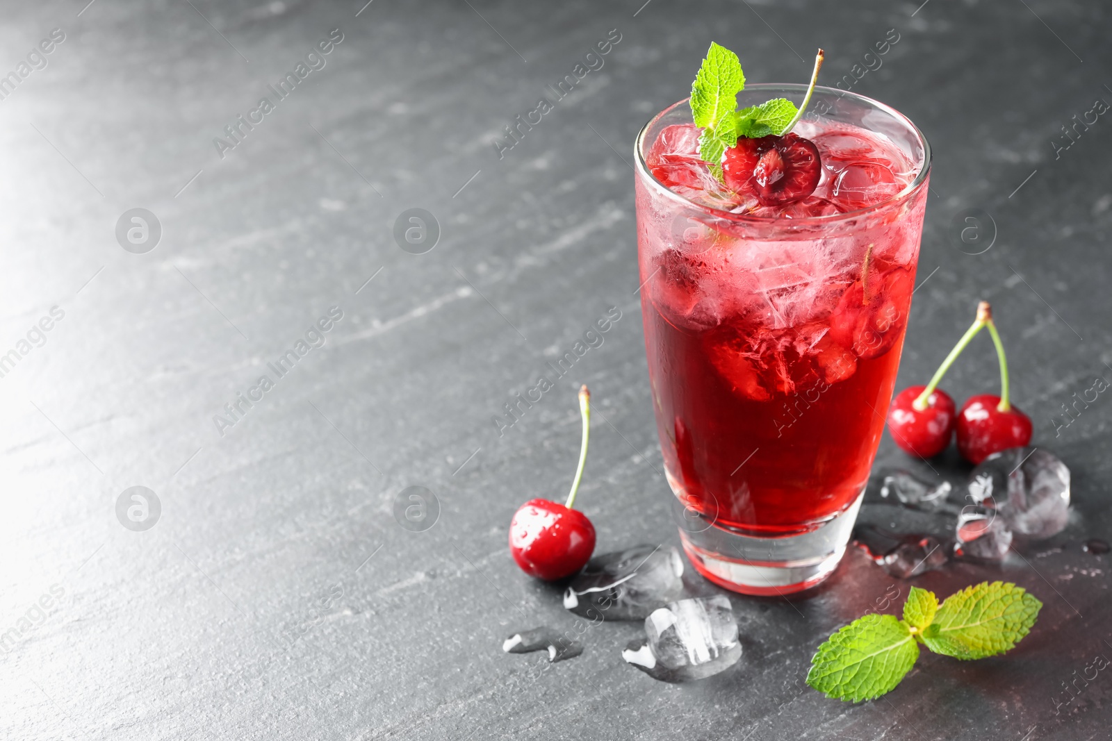 Tasty cherry soda with ice cubes, berries and mint in glass on grey table, closeup. Space for text Photo of Tasty cherry soda with ice cubes, berries and mint in glass on grey table, closeup. Space for text