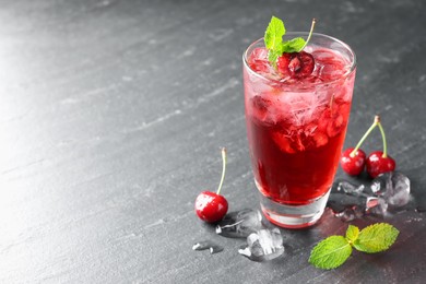 Photo of Tasty cherry soda with ice cubes, berries and mint in glass on grey table, closeup. Space for text