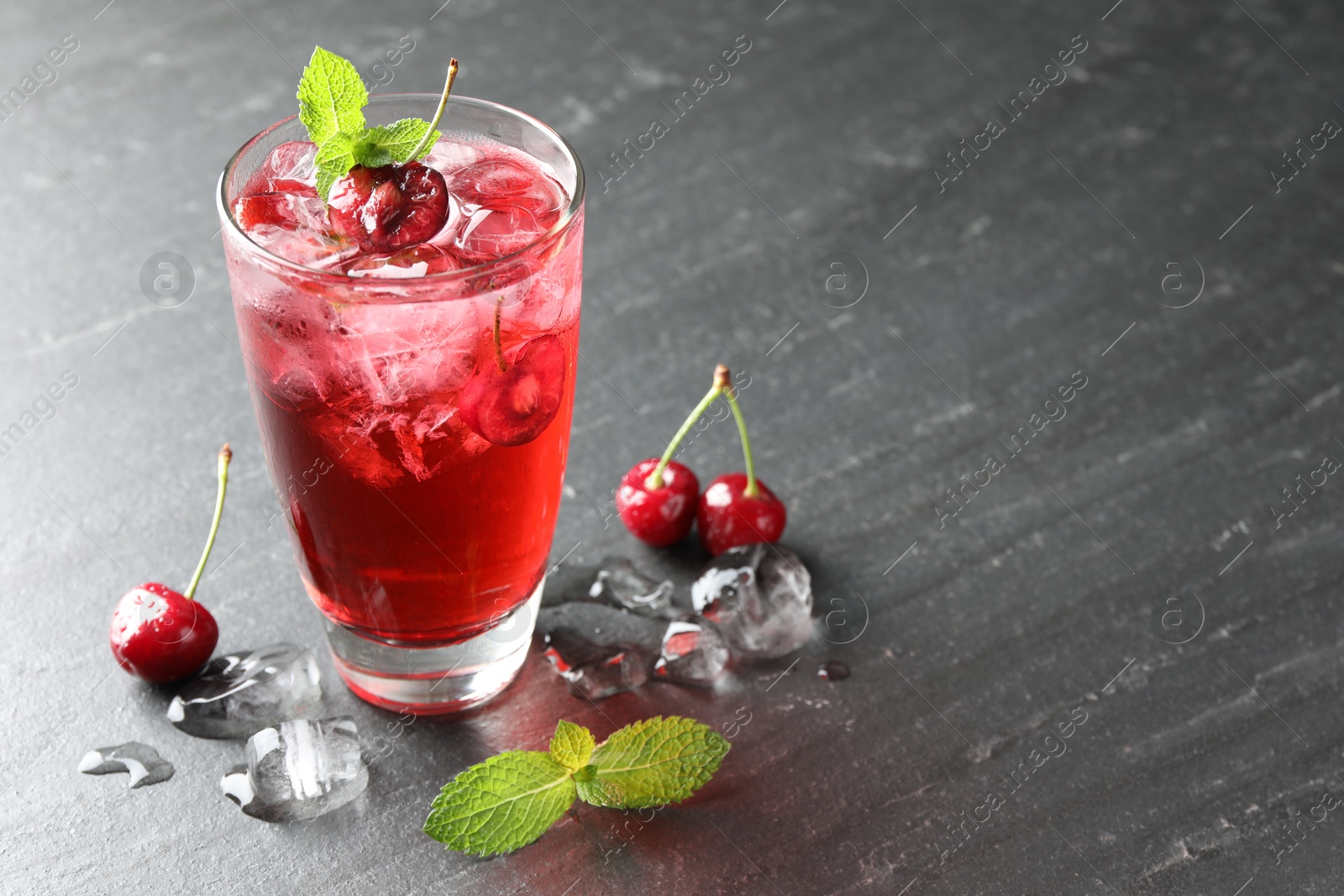 Tasty cherry soda with ice cubes, berries and mint in glass on grey table, closeup. Space for text Photo of Tasty cherry soda with ice cubes, berries and mint in glass on grey table, closeup. Space for text