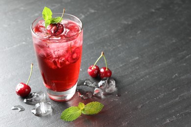 Photo of Tasty cherry soda with ice cubes, berries and mint in glass on grey table, closeup. Space for text