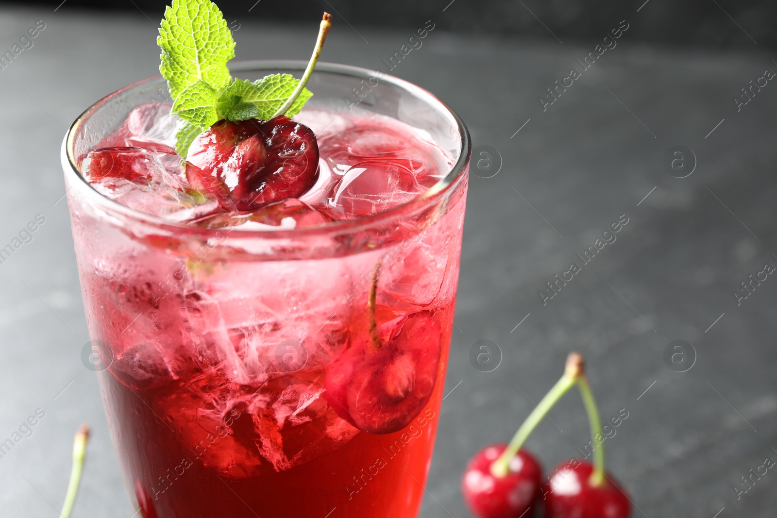 Tasty cherry soda with ice cubes, berries and mint in glass on grey table, closeup. Space for text Photo of Tasty cherry soda with ice cubes, berries and mint in glass on grey table, closeup. Space for text