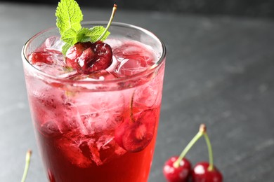 Photo of Tasty cherry soda with ice cubes, berries and mint in glass on grey table, closeup. Space for text