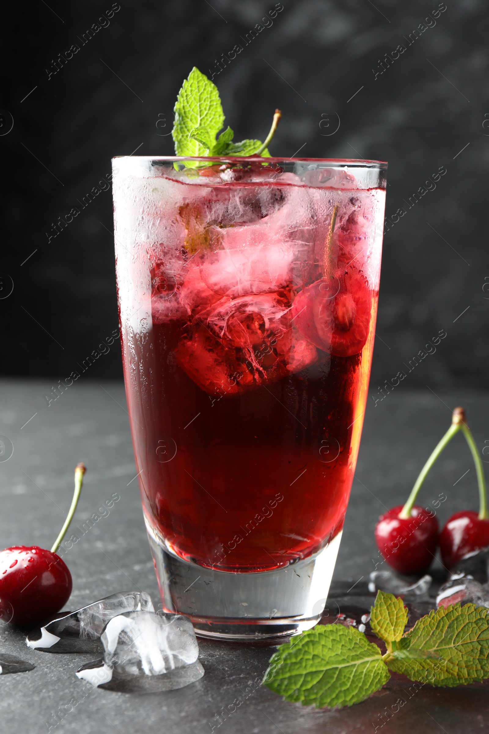 Tasty cherry soda with ice cubes, berries and mint in glass on grey table, closeup Photo of Tasty cherry soda with ice cubes, berries and mint in glass on grey table, closeup