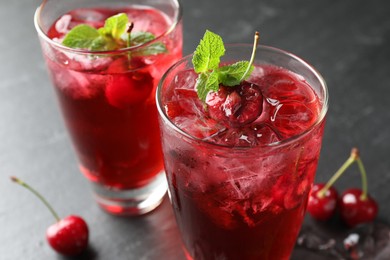 Photo of Tasty cherry soda with ice cubes, berries and mint in glasses on grey table, closeup