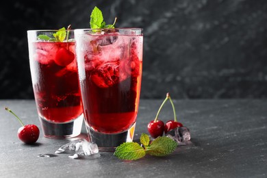 Photo of Tasty cherry soda with ice cubes, berries and mint in glasses on grey table, closeup. Space for text