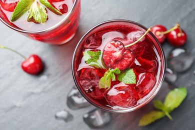 Photo of Tasty cherry soda with ice cubes, berries and mint in glasses on grey table, flat lay