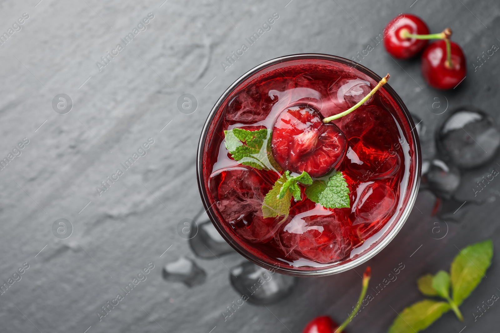 Tasty cherry soda with ice cubes, berries and mint in glass on grey table, flat lay. Space for text Photo of Tasty cherry soda with ice cubes, berries and mint in glass on grey table, flat lay. Space for text