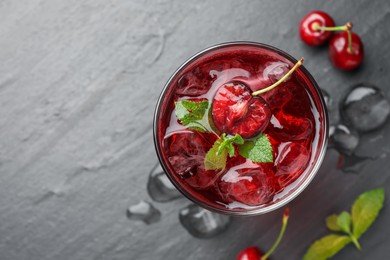 Photo of Tasty cherry soda with ice cubes, berries and mint in glass on grey table, flat lay. Space for text