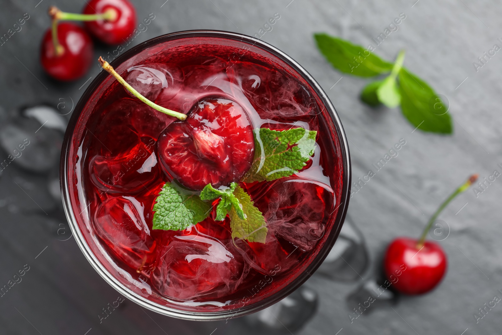 Tasty cherry soda with ice cubes, berries and mint in glass on grey table, flat lay Photo of Tasty cherry soda with ice cubes, berries and mint in glass on grey table, flat lay