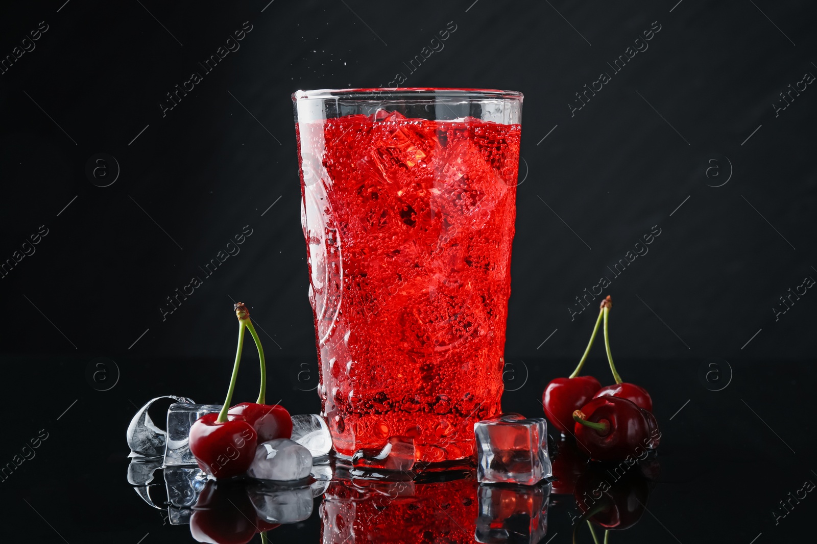 Tasty cherry soda with ice cubes, berries and mint in glass on black background, closeup Photo of Tasty cherry soda with ice cubes, berries and mint in glass on black background, closeup