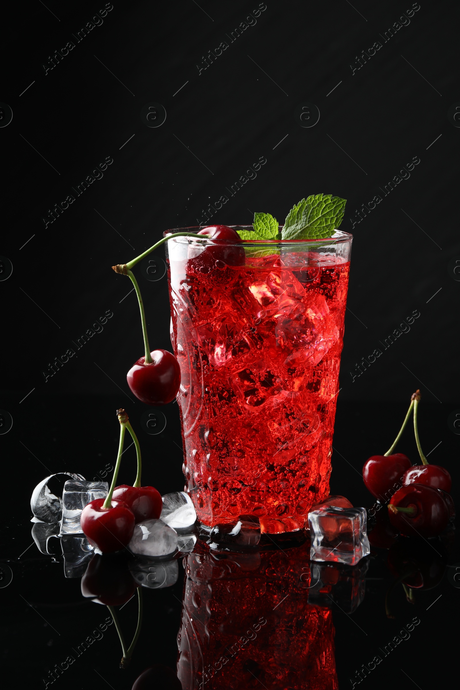 Tasty cherry soda with ice cubes, berries and mint in glass on black background, closeup Photo of Tasty cherry soda with ice cubes, berries and mint in glass on black background, closeup