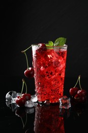 Photo of Tasty cherry soda with ice cubes, berries and mint in glass on black background, closeup