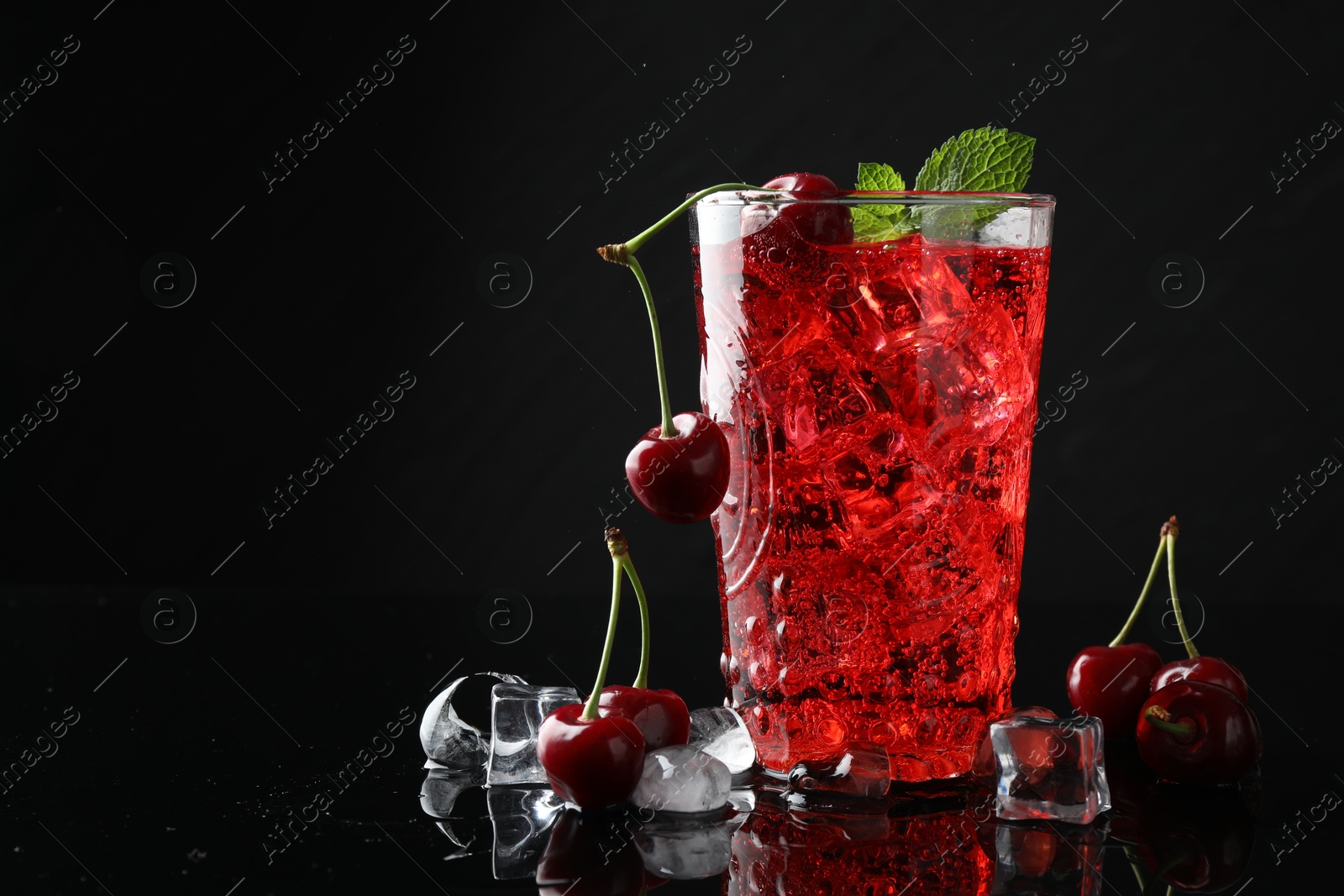 Tasty cherry soda with ice cubes, berries and mint in glass on black background, closeup. Space for text Photo of Tasty cherry soda with ice cubes, berries and mint in glass on black background, closeup. Space for text