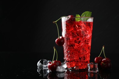 Photo of Tasty cherry soda with ice cubes, berries and mint in glass on black background, closeup. Space for text