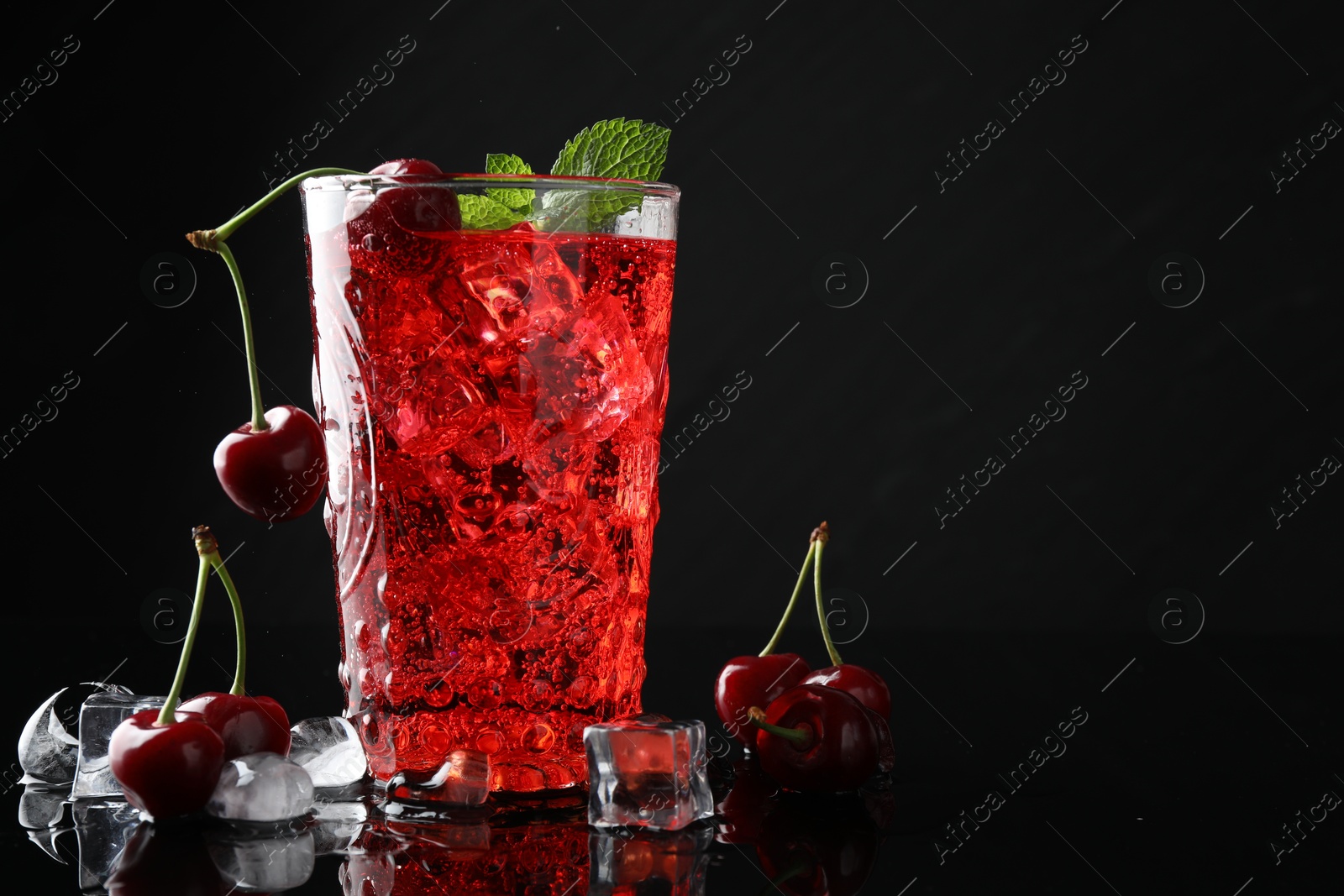 Tasty cherry soda with ice cubes, berries and mint in glass on black background, closeup. Space for text Photo of Tasty cherry soda with ice cubes, berries and mint in glass on black background, closeup. Space for text