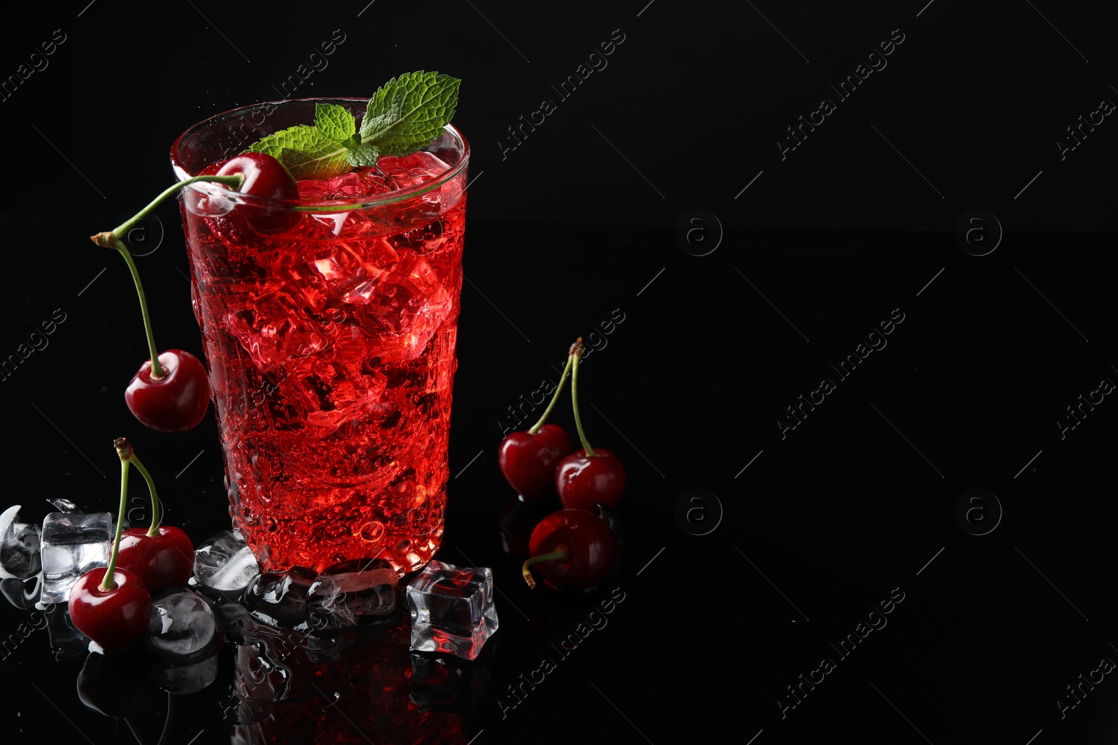 Tasty cherry soda with ice cubes, berries and mint in glass on black background, closeup. Space for text Photo of Tasty cherry soda with ice cubes, berries and mint in glass on black background, closeup. Space for text