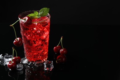 Photo of Tasty cherry soda with ice cubes, berries and mint in glass on black background, closeup. Space for text