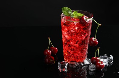 Photo of Tasty cherry soda with ice cubes, berries and mint in glass on black background, closeup. Space for text