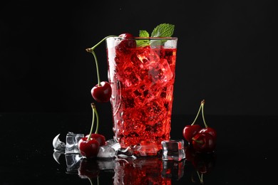 Photo of Tasty cherry soda with ice cubes, berries and mint in glass on black background, closeup